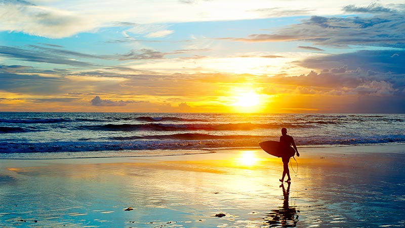 Surfer walks across the beach in a popular tourist place in Bali